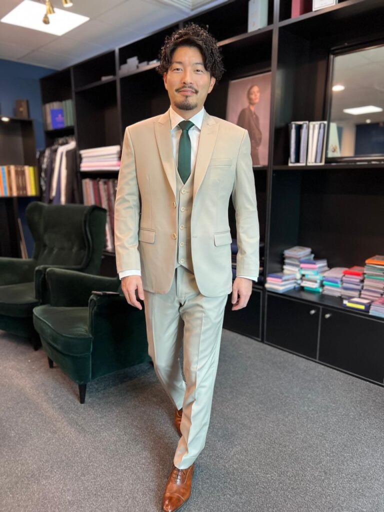 A man dressed in a beige color suit with green color tie