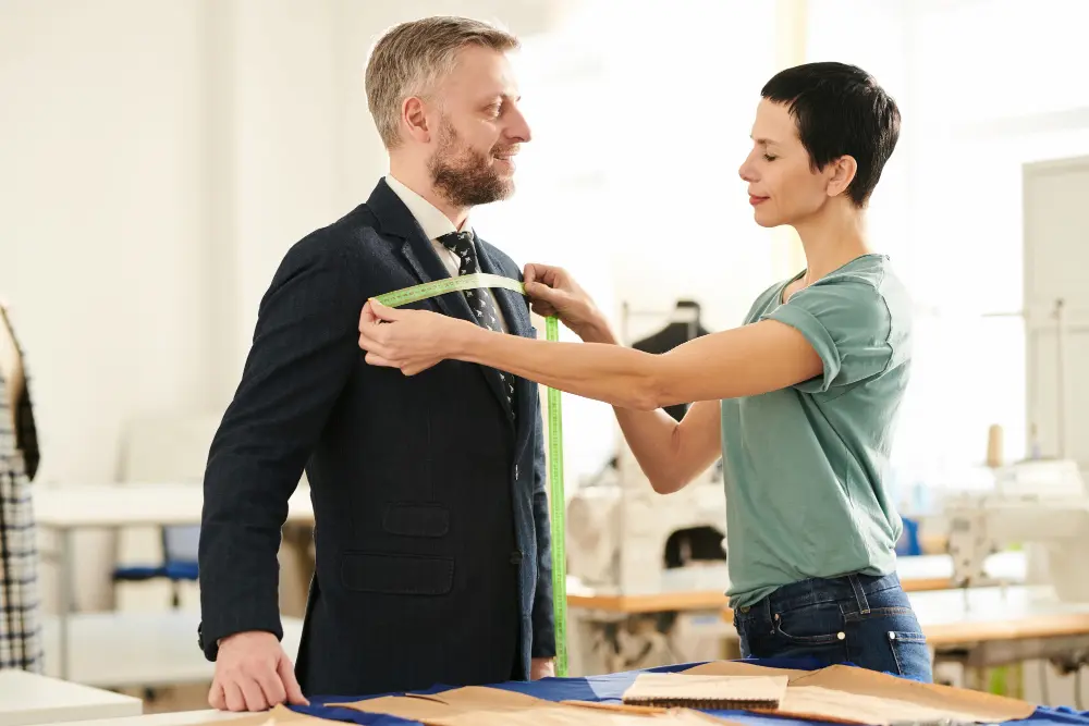 Bespoke tailor measuring a client in a contemporary office environment.
